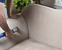 Professional upholstery cleaner deep-cleaning a fabric sofa with a handheld extraction tool and hose in Tacoma, WA.